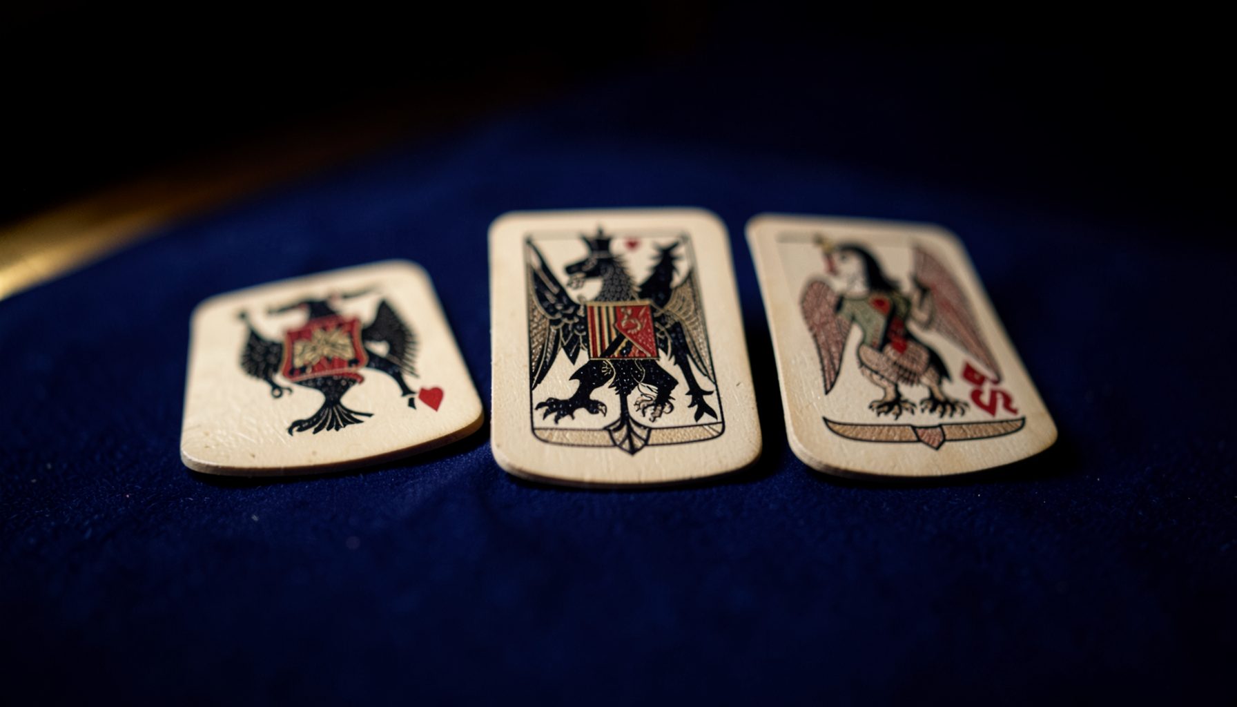 Three aces glowing under warm golden light on a deep indigo table, premium and intense card-game atmosphere