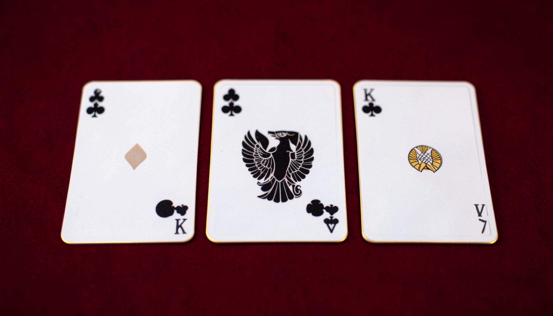 Three playing cards arranged in a neat row on a rich burgundy surface with soft golden highlights